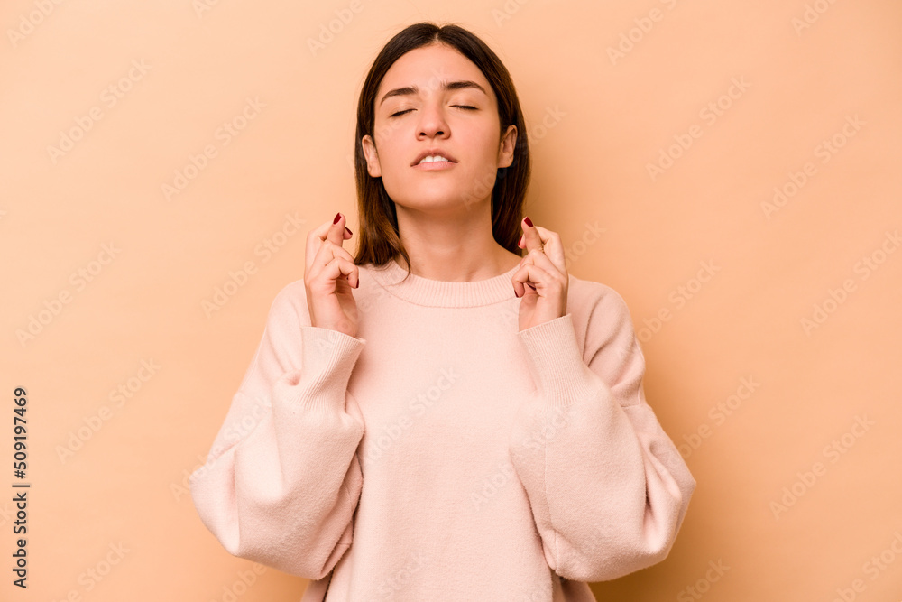 Obraz premium Young hispanic woman isolated on beige background crossing fingers for having luck