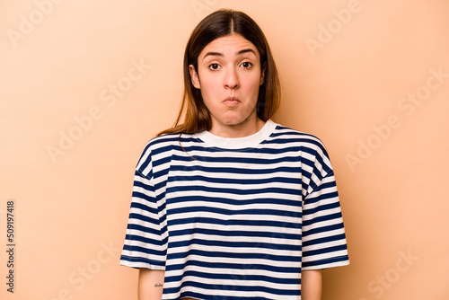 Young hispanic woman isolated on beige background shrugs shoulders and open eyes confused. © Asier