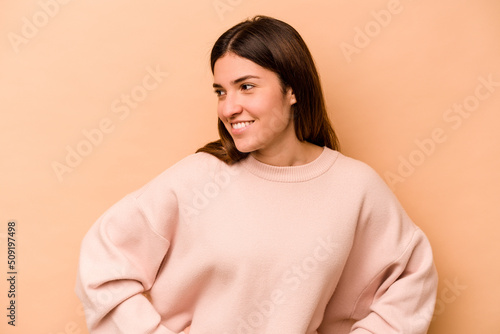 Young hispanic woman isolated on beige background confident keeping hands on hips. © Asier