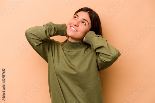 Young hispanic woman isolated on beige background feeling confident, with hands behind the head. © Asier