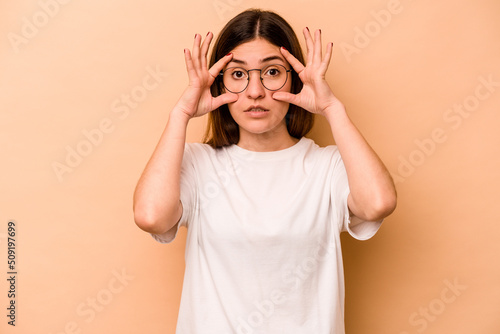 Young hispanic woman isolated on beige background keeping eyes opened to find a success opportunity.