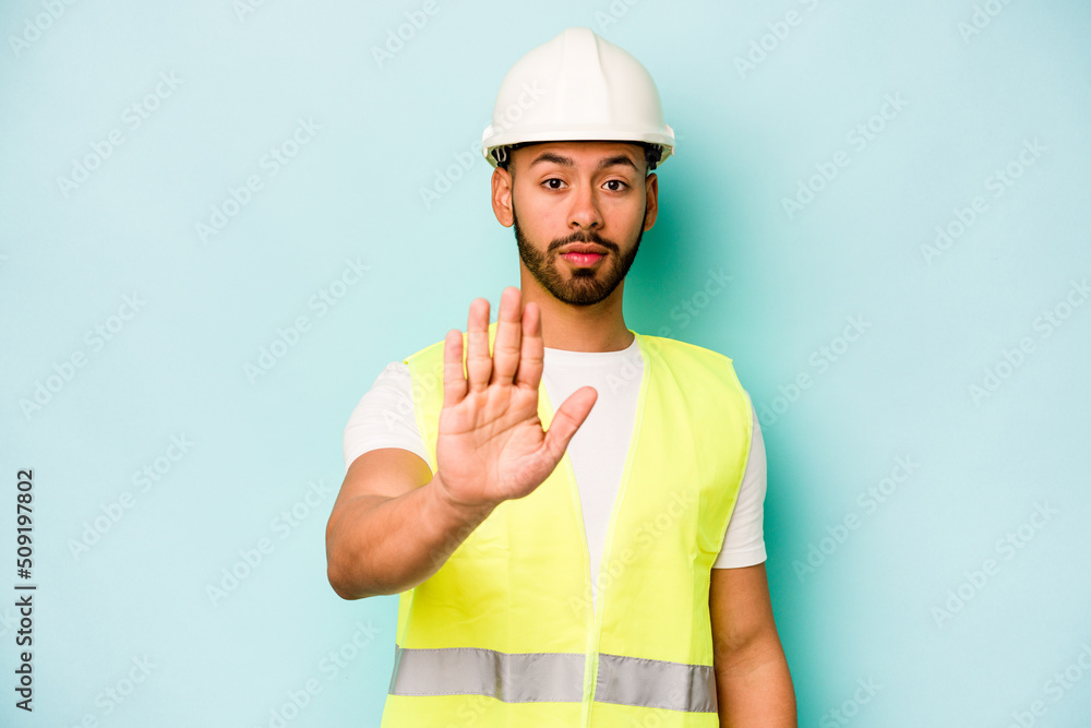 Young laborer hispanic man isolated on blue background standing with outstretched hand showing stop sign, preventing you.