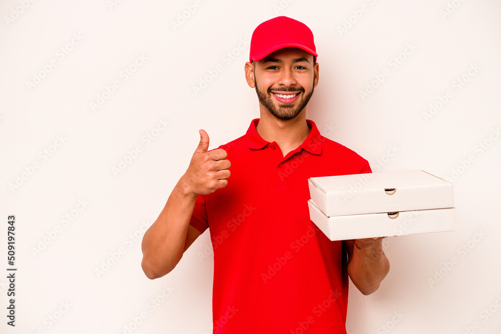 Young hispanic delivery man holding pizzas isolated on white background smiling and raising thumb up Young hispanic delivery man holding pizzas isolated on white background smiling and raising thumb up