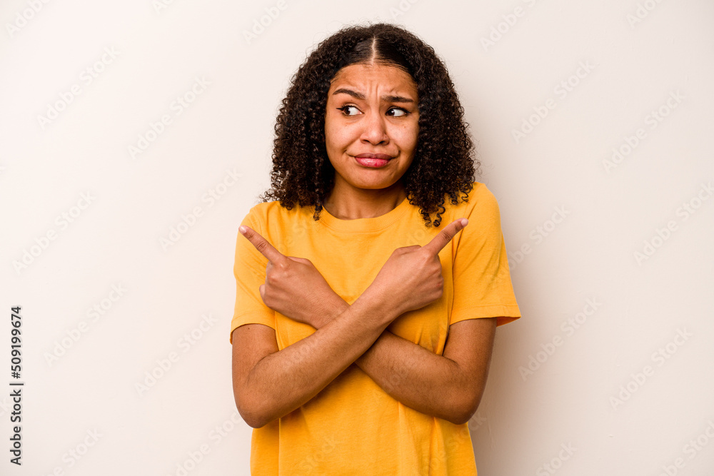 Young African American woman isolated on white background points sideways, is trying to choose between two options. Young African American woman isolated on white background points sideways, is trying to choose between two options.