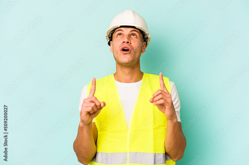 Young laborer caucasian man isolated on blue background pointing upside with opened mouth. Young laborer caucasian man isolated on blue background pointing upside with opened mouth.