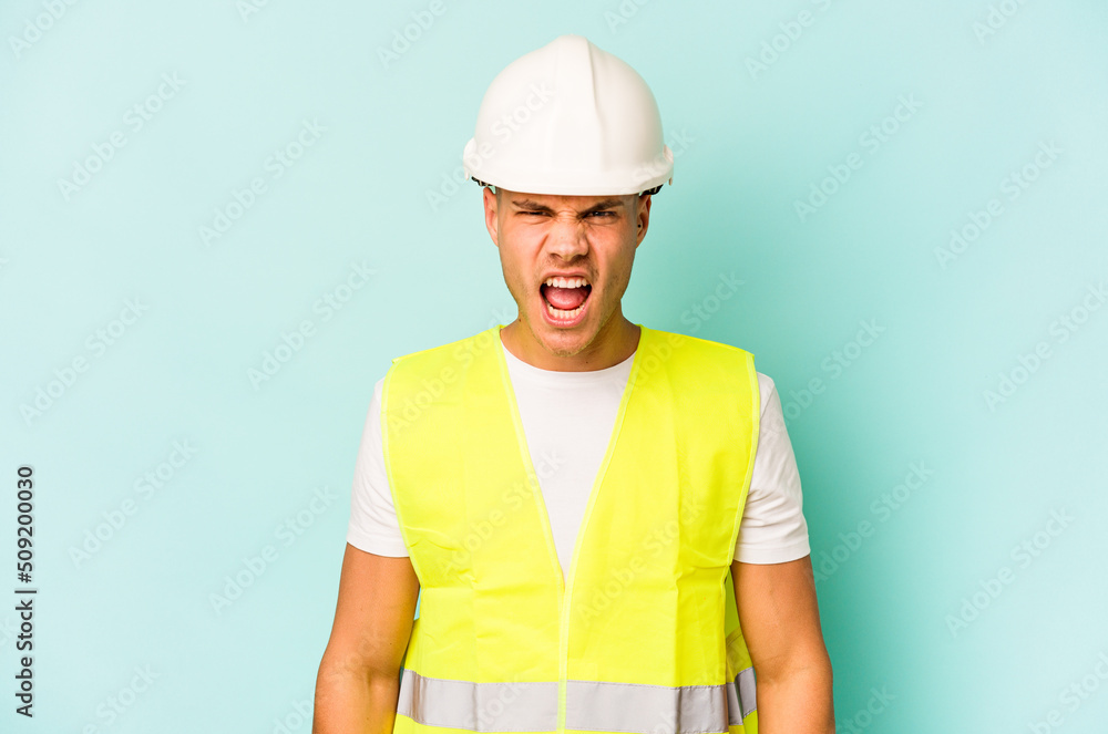 Young laborer caucasian man isolated on blue background screaming very angry and aggressive.
