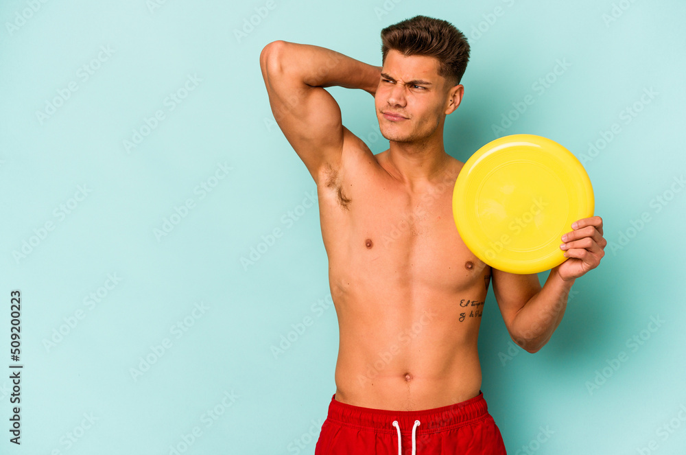 Young caucasian man playing with frisky isolated on blue background touching back of head, thinking and making a choice.