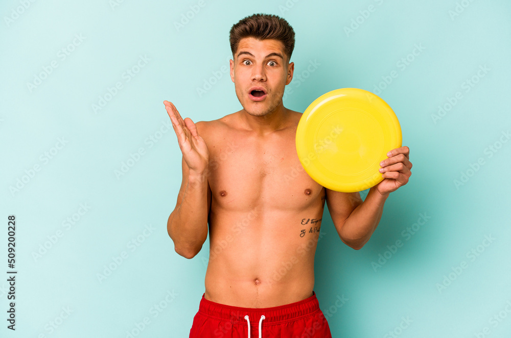 Young caucasian man playing with frisky isolated on blue background surprised and shocked.