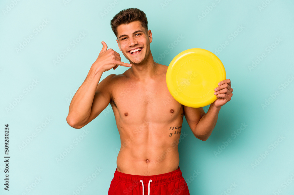 Young caucasian man playing with frisky isolated on blue background showing a mobile phone call gesture with fingers.