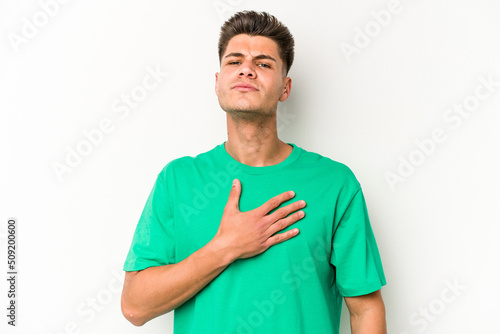 Young caucasian man isolated on white background taking an oath, putting hand on chest. © Asier