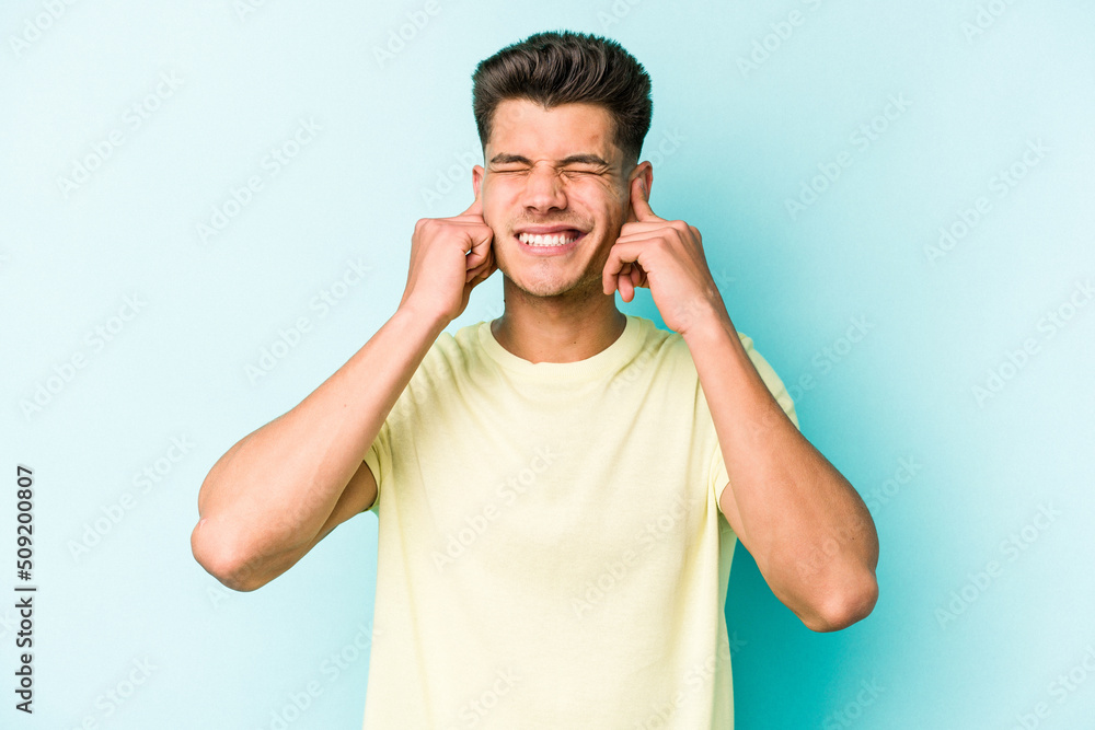 Young caucasian man isolated on blue background covering ears with fingers, stressed and desperate by a loudly ambient. Young caucasian man isolated on blue background covering ears with fingers, stressed and desperate by a loudly ambient.