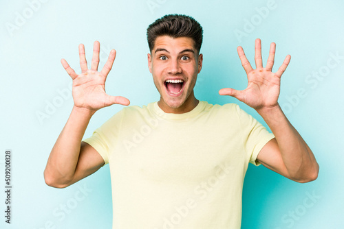 Young caucasian man isolated on blue background receiving a pleasant surprise, excited and raising hands. © Asier