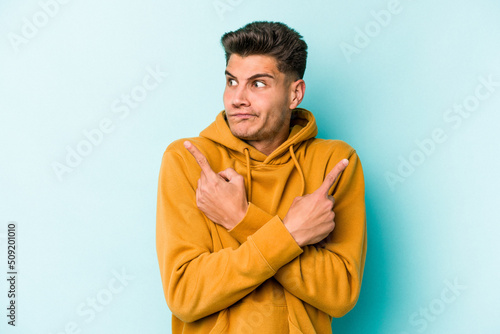 Young caucasian man isolated on blue background points sideways, is trying to choose between two options.