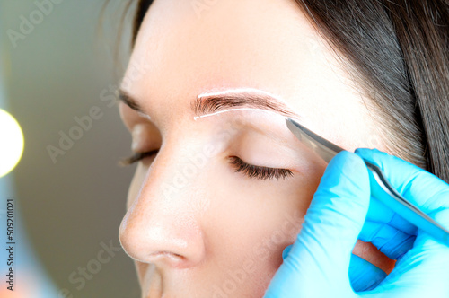 Eyebrow correction or eyebrow shaping treatment using tweezers close-up view.