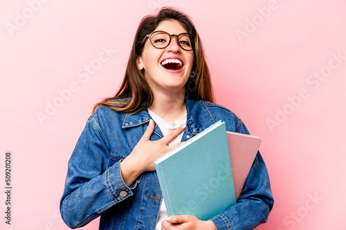 Young student caucasian woman isolated on pink background laughs out loudly keeping hand on chest.