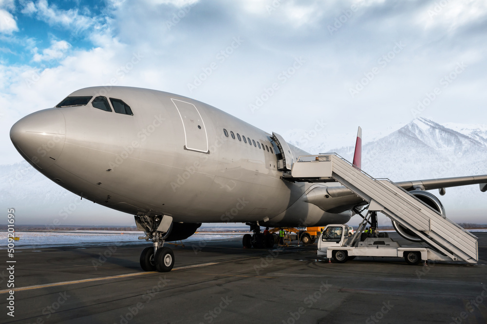 Wide body passenger airplane and aircraft steps at the airport apron on the background of high scenic snow-capped mountains