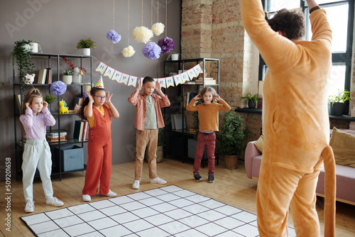 Group of children playing and dancing with animator in animal costume during birthday party at home