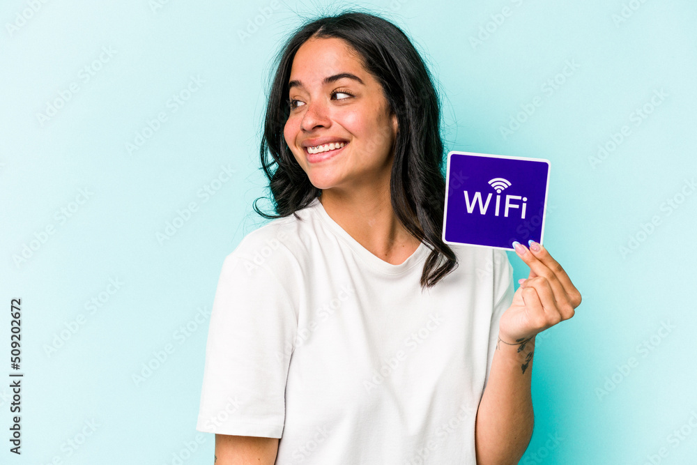 Young hispanic woman holding wifi placard isolated on yellow background looks aside smiling, cheerful and pleasant. Young hispanic woman holding wifi placard isolated on yellow background looks aside smiling, cheerful and pleasant.