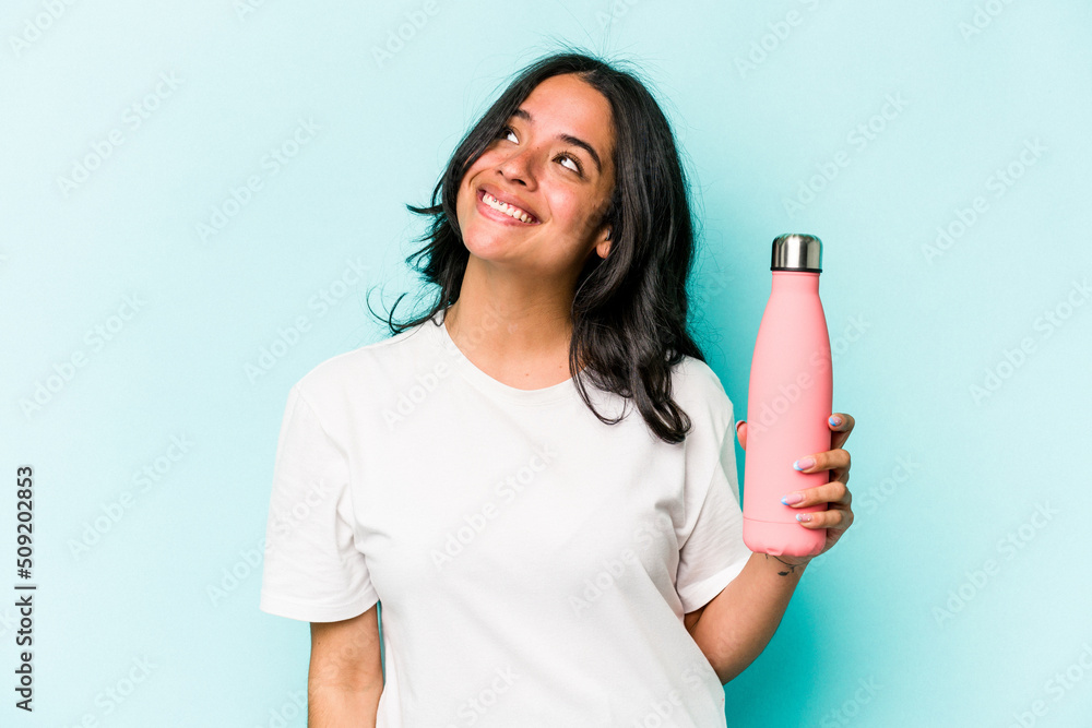 Young hispanic woman holding thermo isolated on blue background dreaming of achieving goals and purposes Young hispanic woman holding thermo isolated on blue background dreaming of achieving goals and purposes