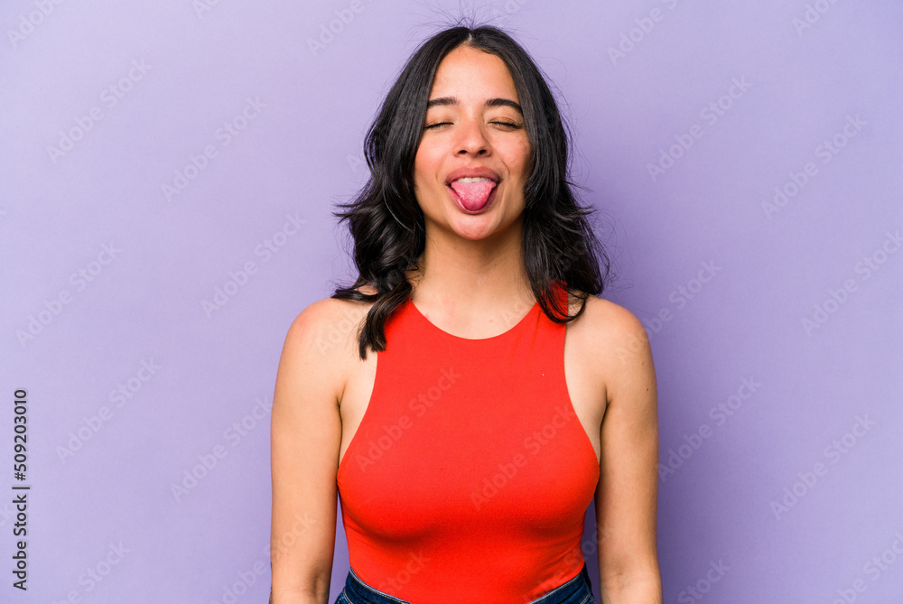 Young hispanic woman isolated on purple background funny and friendly sticking out tongue. Young hispanic woman isolated on purple background funny and friendly sticking out tongue.