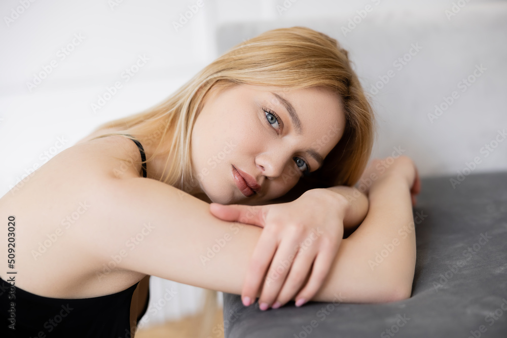 Portrait of blonde woman looking at camera near blurred couch. Portrait of blonde woman looking at camera near blurred couch.
