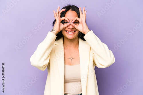 Young hispanic woman isolated on purple background excited keeping ok gesture on eye.