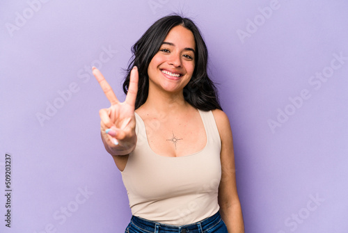 Young hispanic woman isolated on purple background joyful and carefree showing a peace symbol with fingers. © Asier