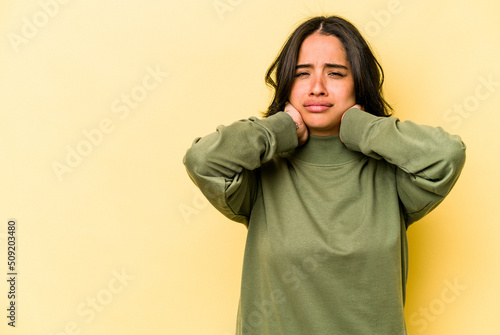 Young hispanic woman isolated on yellow background touching back of head, thinking and making a choice. © Asier