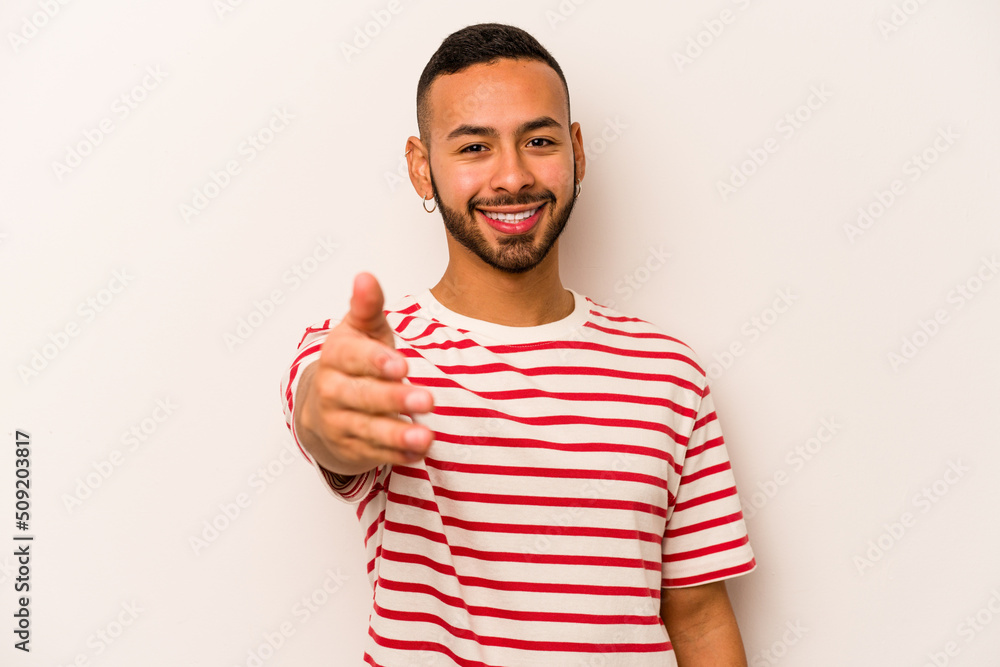 Fototapeta premium Young hispanic man isolated on white background stretching hand at camera in greeting gesture.