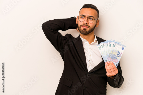 Young business hispanic man holding banknotes isolated on white background touching back of head, thinking and making a choice.
