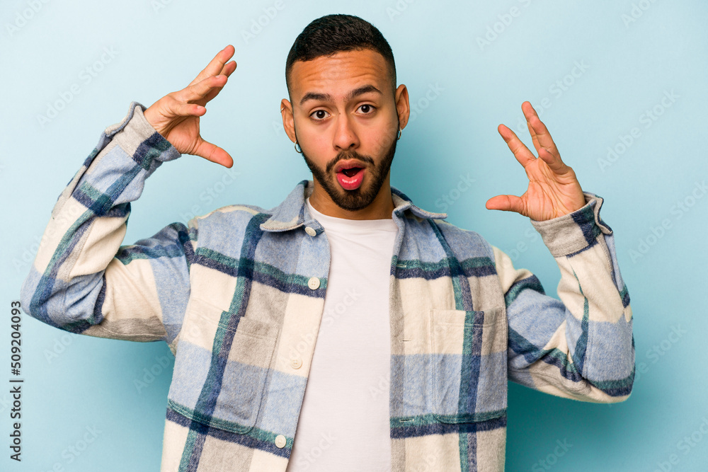 Naklejka premium Young hispanic man isolated on blue background celebrating a victory or success, he is surprised and shocked.