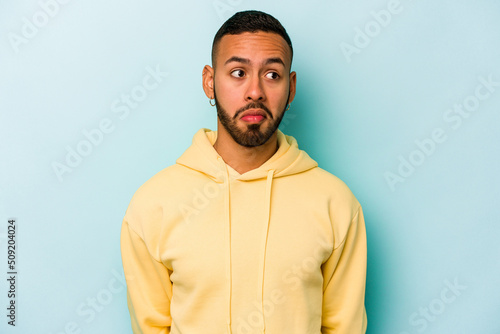 Young hispanic man isolated on blue background confused, feels doubtful and unsure.
