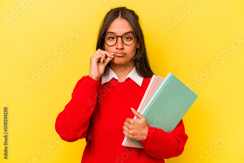 Young student hispanic woman isolated on yellow background with fingers on lips keeping a secret.