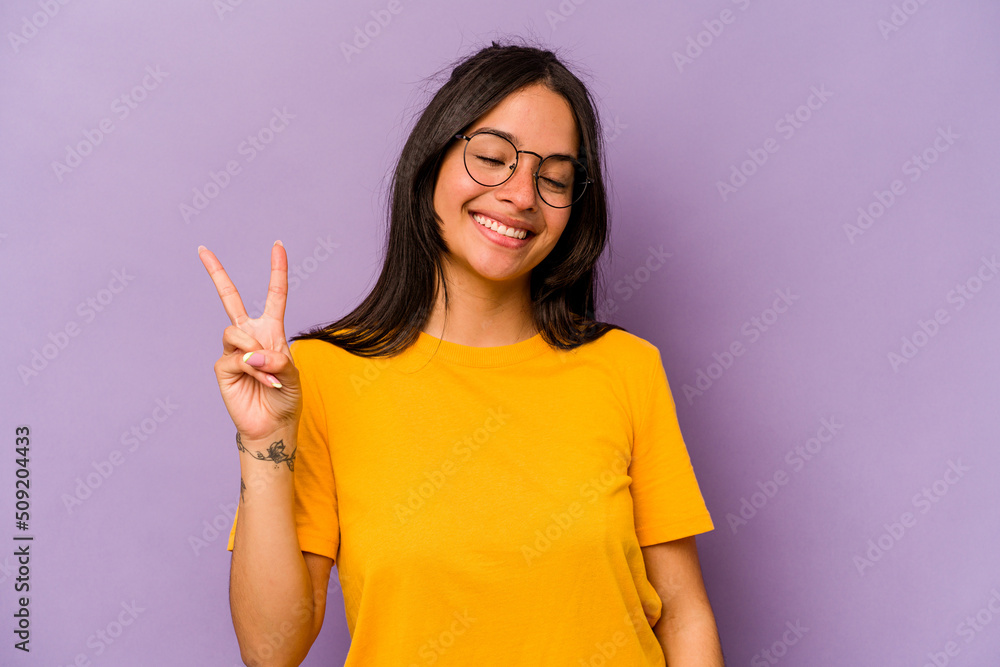 Young hispanic woman isolated on purple background joyful and carefree showing a peace symbol with fingers. Young hispanic woman isolated on purple background joyful and carefree showing a peace symbol with fingers.