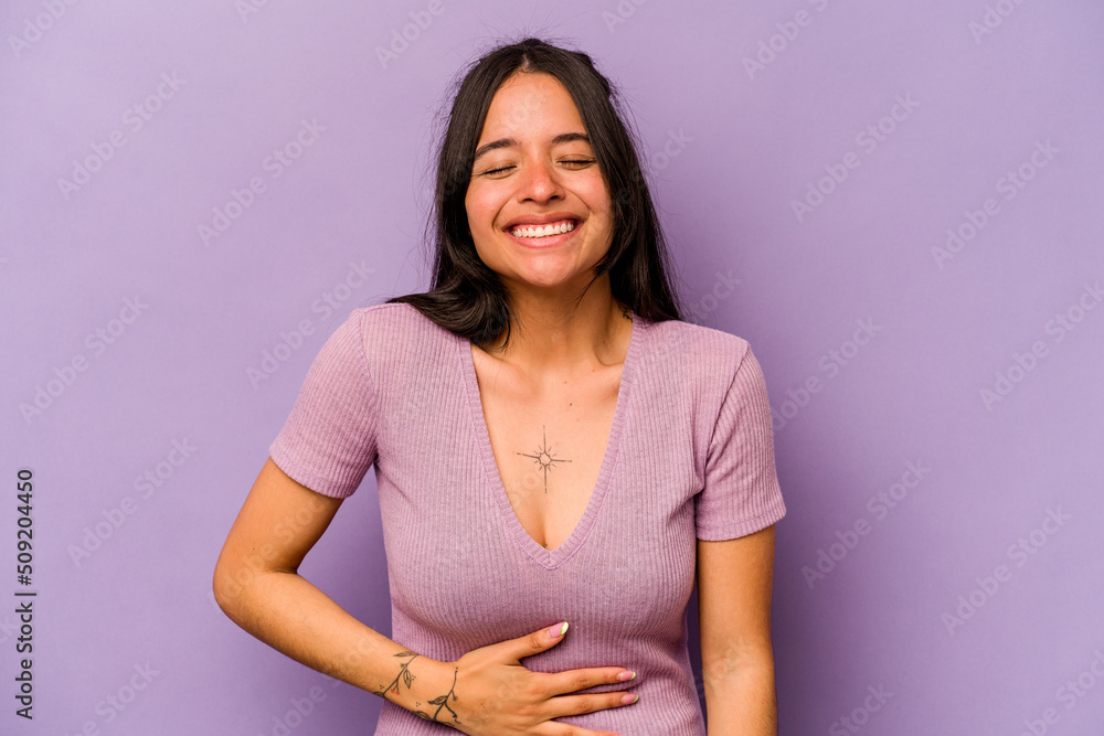 Fototapeta premium Young hispanic woman isolated on purple background touches tummy, smiles gently, eating and satisfaction concept.