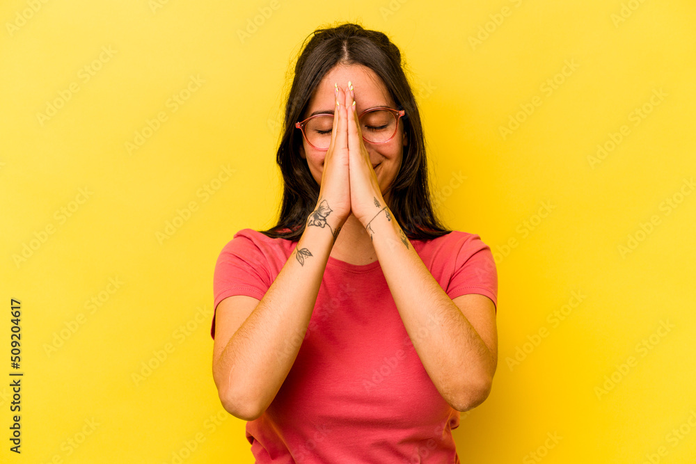 Young hispanic woman isolated on yellow background holding hands in pray near mouth, feels confident. Young hispanic woman isolated on yellow background holding hands in pray near mouth, feels confident.