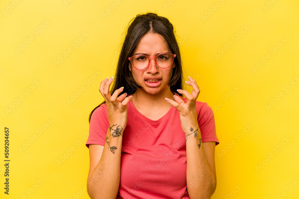 Young hispanic woman isolated on yellow background upset screaming with tense hands. Young hispanic woman isolated on yellow background upset screaming with tense hands.
