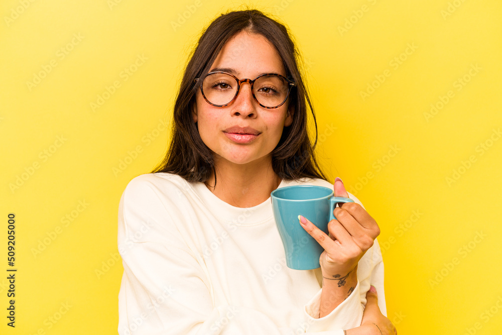 Young hispanic woman holding a mug isolated on yellow background Young hispanic woman holding a mug isolated on yellow background