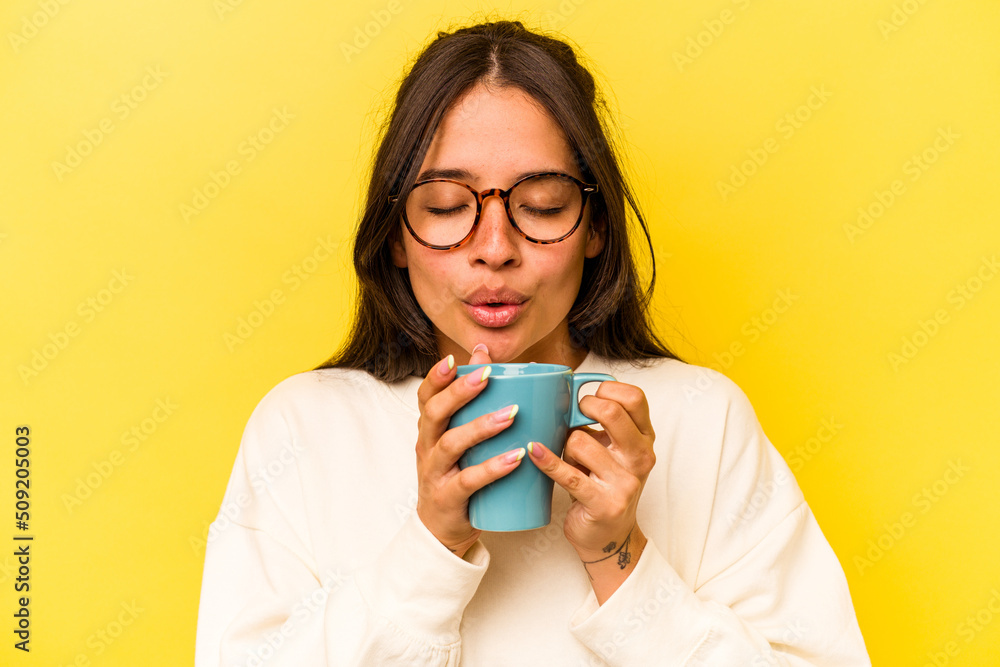 Young hispanic woman holding a mug isolated on yellow background Young hispanic woman holding a mug isolated on yellow background