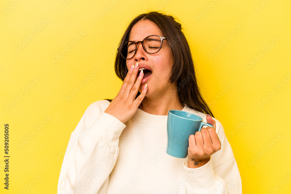 Young hispanic woman holding a mug isolated on yellow background Young hispanic woman holding a mug isolated on yellow background