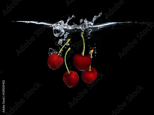 Red sweet cherries under water isolated on black background