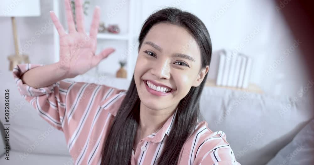 Smiling Asian woman happily sits in the living room and enjoys taking selfies. Smiling Asian woman happily sits in the living room and enjoys taking selfies.