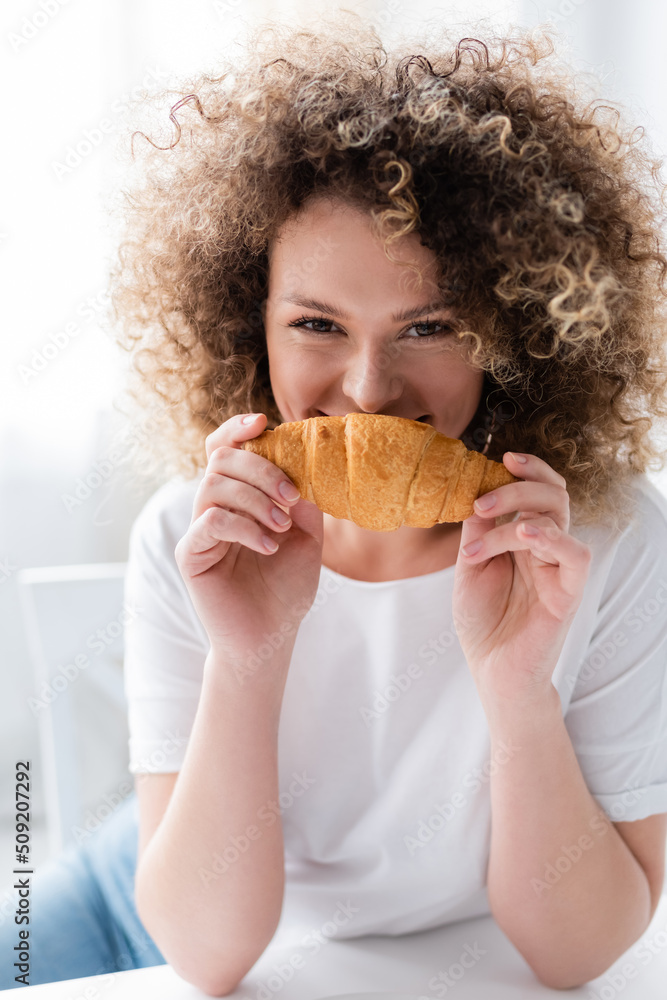 pleased woman with wavy hair smelling delicious croissant and looking at camera. pleased woman with wavy hair smelling delicious croissant and looking at camera.