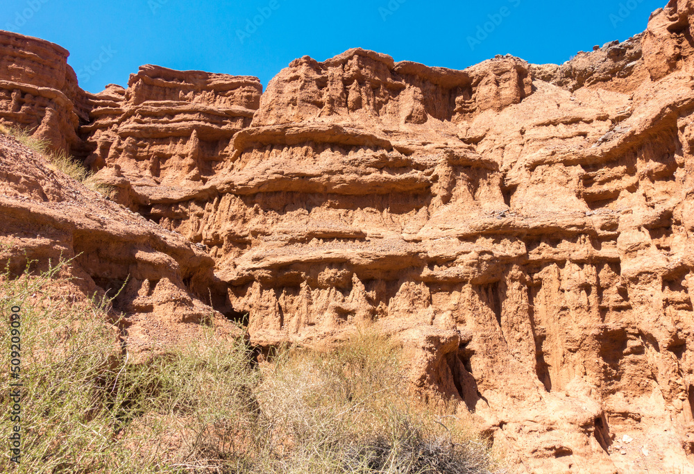Fototapeta premium Red tales from clay. Issyk-Kul region in Kyrgyzstan. Beautiful mountain landscape. Tourism and travel.