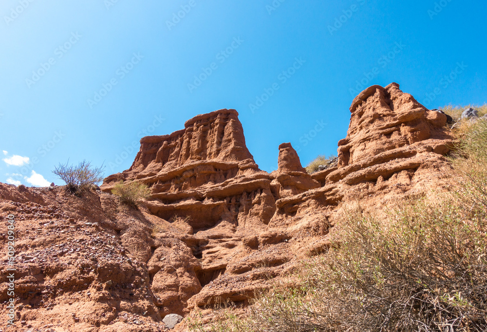 Fototapeta premium Red tales from clay. Issyk-Kul region in Kyrgyzstan. Beautiful mountain landscape. Tourism and travel.