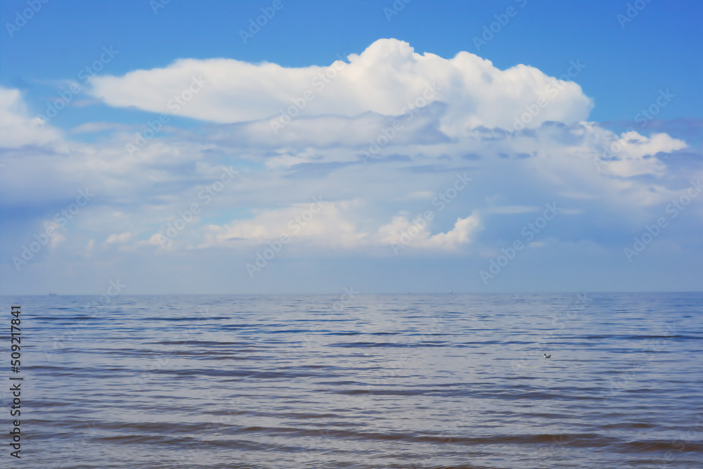 White clouds on blue sky over calm Baltic sea with sunlight reflection in sea. Nature shot in Latvia