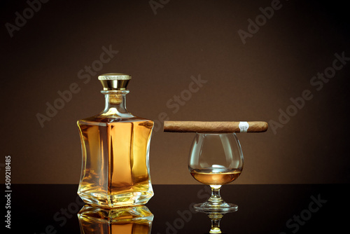 close up view of cigar, bottle of whiskey and  glass aside on color back. 