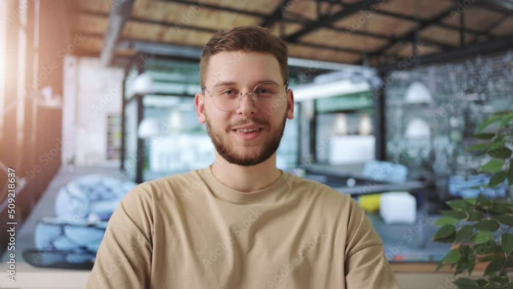 Happy male employee in trendy eyeglasses sitting at desk with sincere smile on face. Caucasian young man working with joy in empty modern office room. Happy male employee in trendy eyeglasses sitting at desk with sincere smile on face. Caucasian young man working with joy in empty modern office room.
