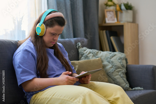 Young female with disability watching online video or movie while relaxing on comfortable couch at leisure in living room