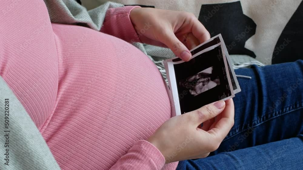Pregnant woman touching her belly while viewing ultrasound scans at home, pregnancy, and childbirth